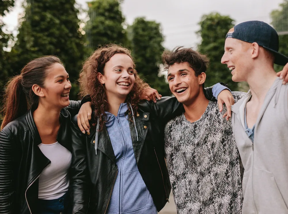 Portrait of multiracial group of people enjoying outdoors. Four young friends standing together and smiling.